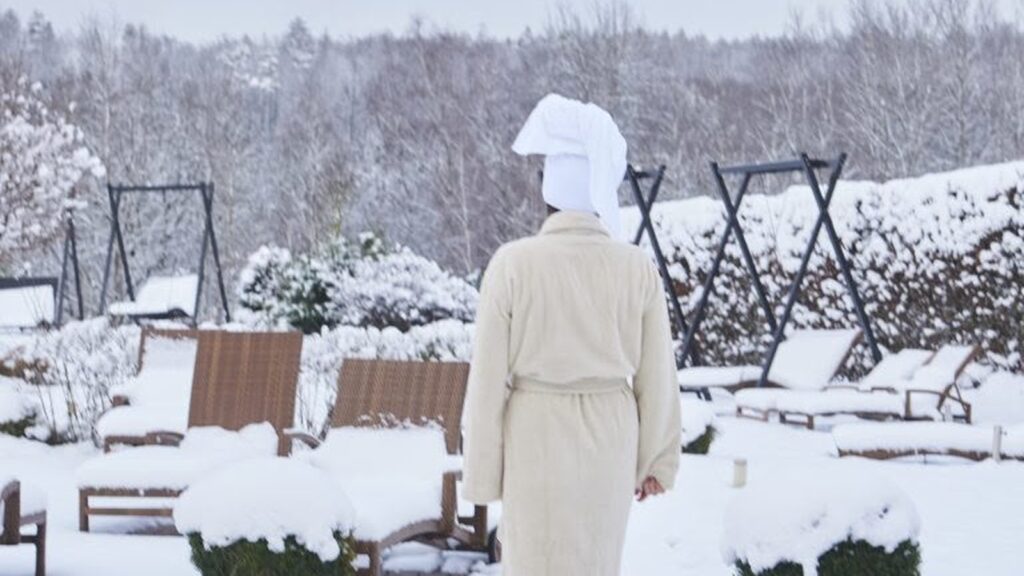 Frau im Bademantel geht durch den verschneiten Garten des Hotel Heinz